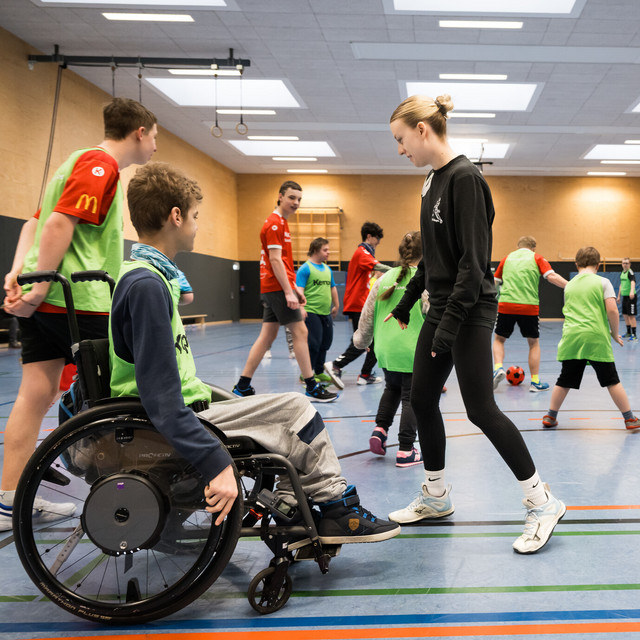 Kinder und Jugendliche mit und ohne Behinderung spielen gemeinsam Fußball in einer Sporthalle