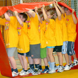 Mehrere Kinder spielen unter einer Gummimatte.
